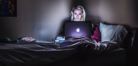 Frau arbeitet nachts im Bett sitzend an einem Laptop.